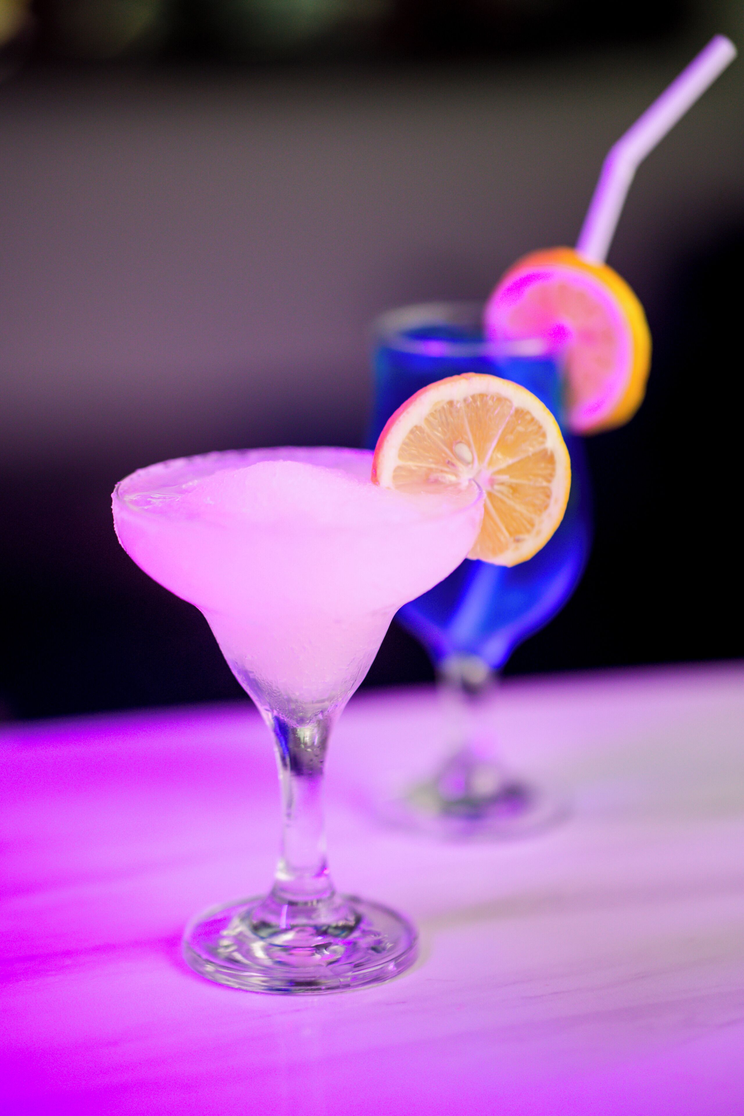 Zwei Cocktails in Martini-Gläsern vor einem violetten Hintergrund.