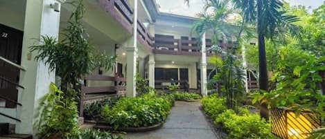 A building with a covered walkway, surrounded by lush greenery and palm trees.