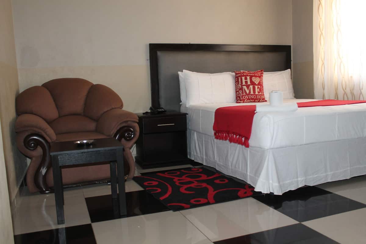 Habitación de hotel con cama, una silla, una mesita de noche y un tapete con estampado rojo y negro.