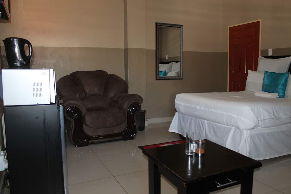 Una habitación de hotel con cama, una silla, una mesa, un refrigerador y un espejo.