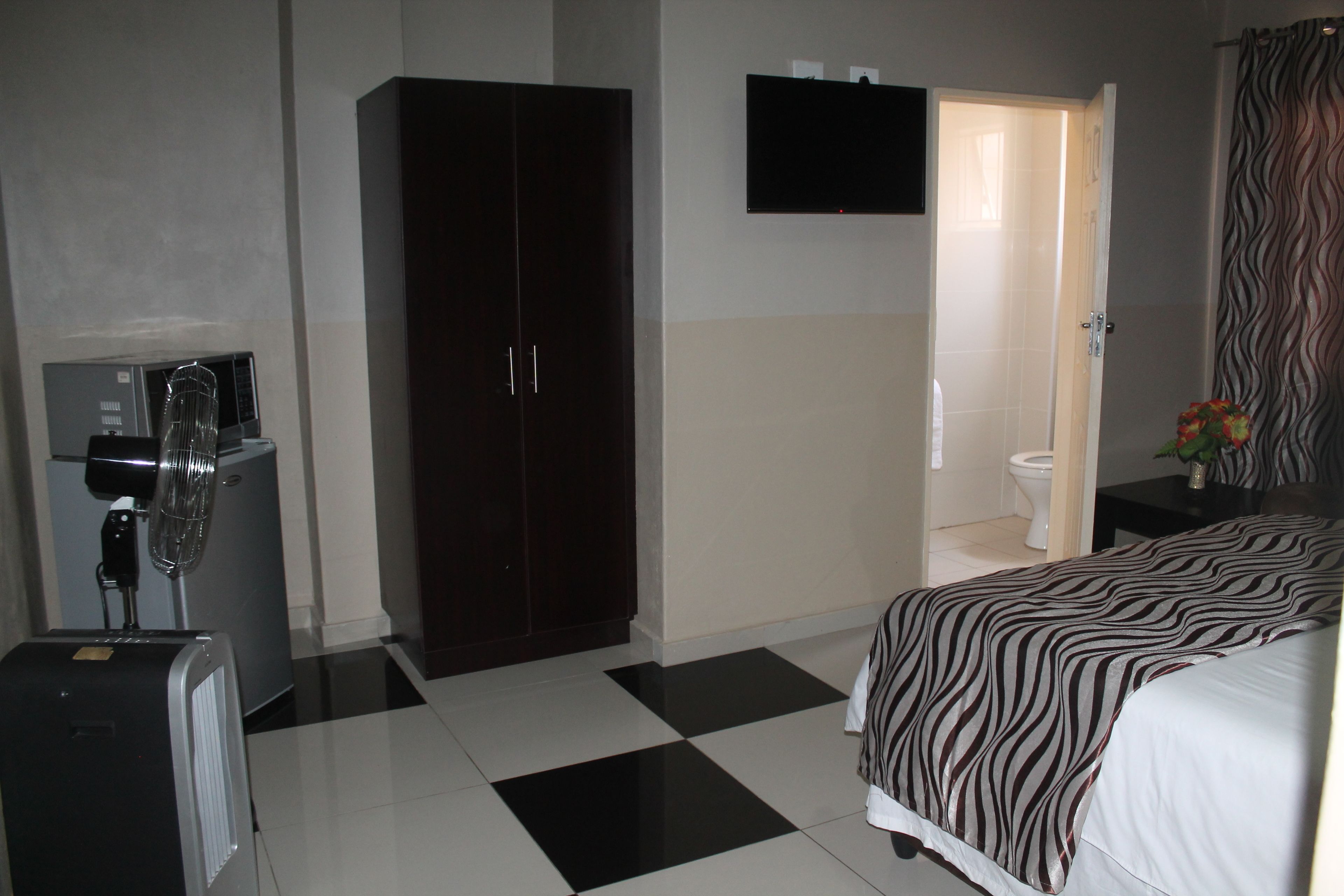 Habitación de hotel con cama, armario, escritorio con silla, televisor y baño visible a través de una puerta abierta.