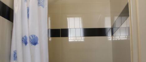 A bathroom with a shower curtain featuring blue scallop shell patterns, a white sink, and beige tiled walls.
