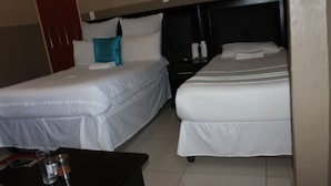 Ein Hotelzimmer mit zwei Betten, einem Nachttisch, einem kleinen Tisch mit einem Glas und einer Flasche sowie einer roten Tür.