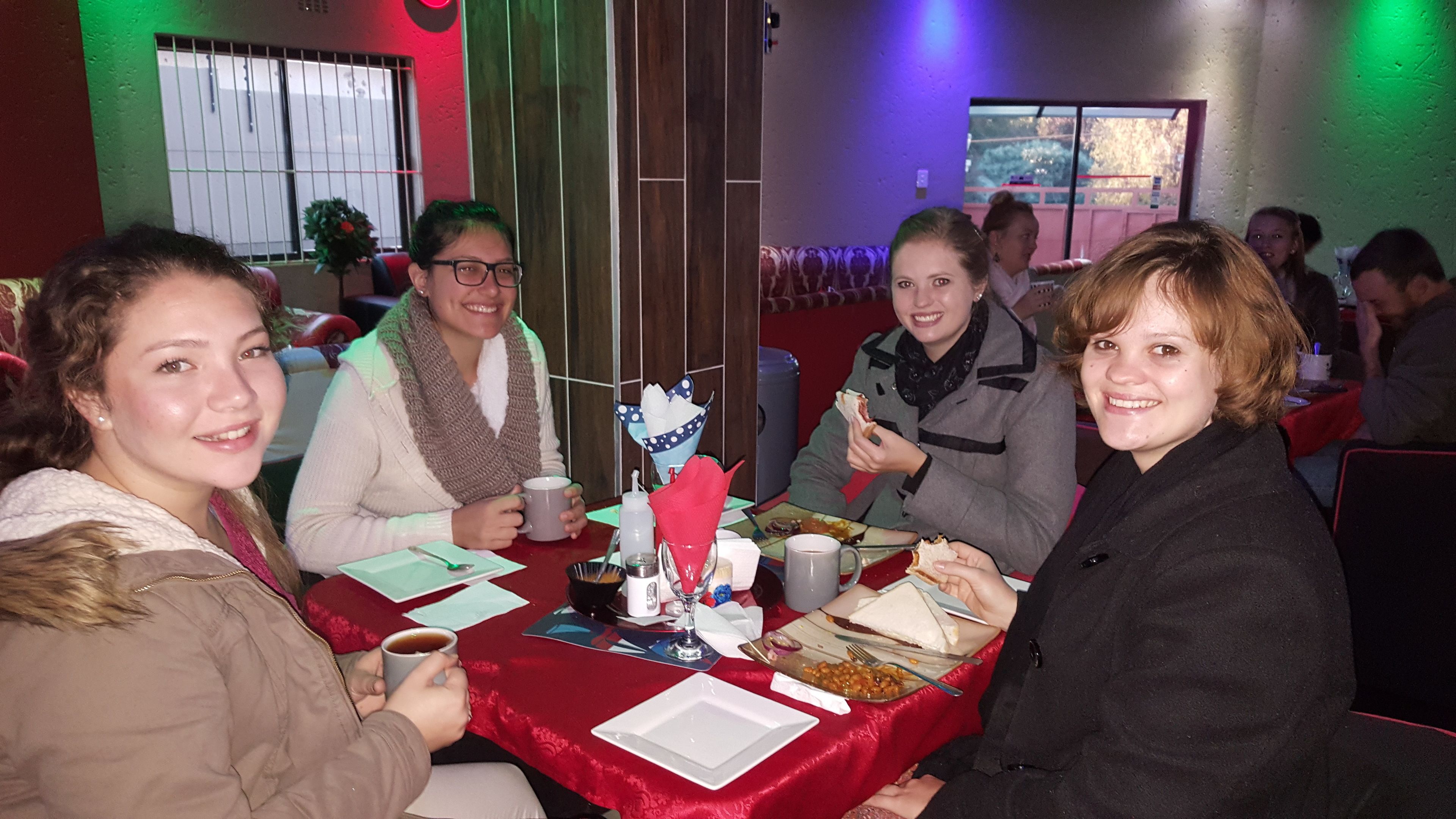 Un grupo de personas sentadas a una mesa con mantel rojo, disfrutando de una comida.