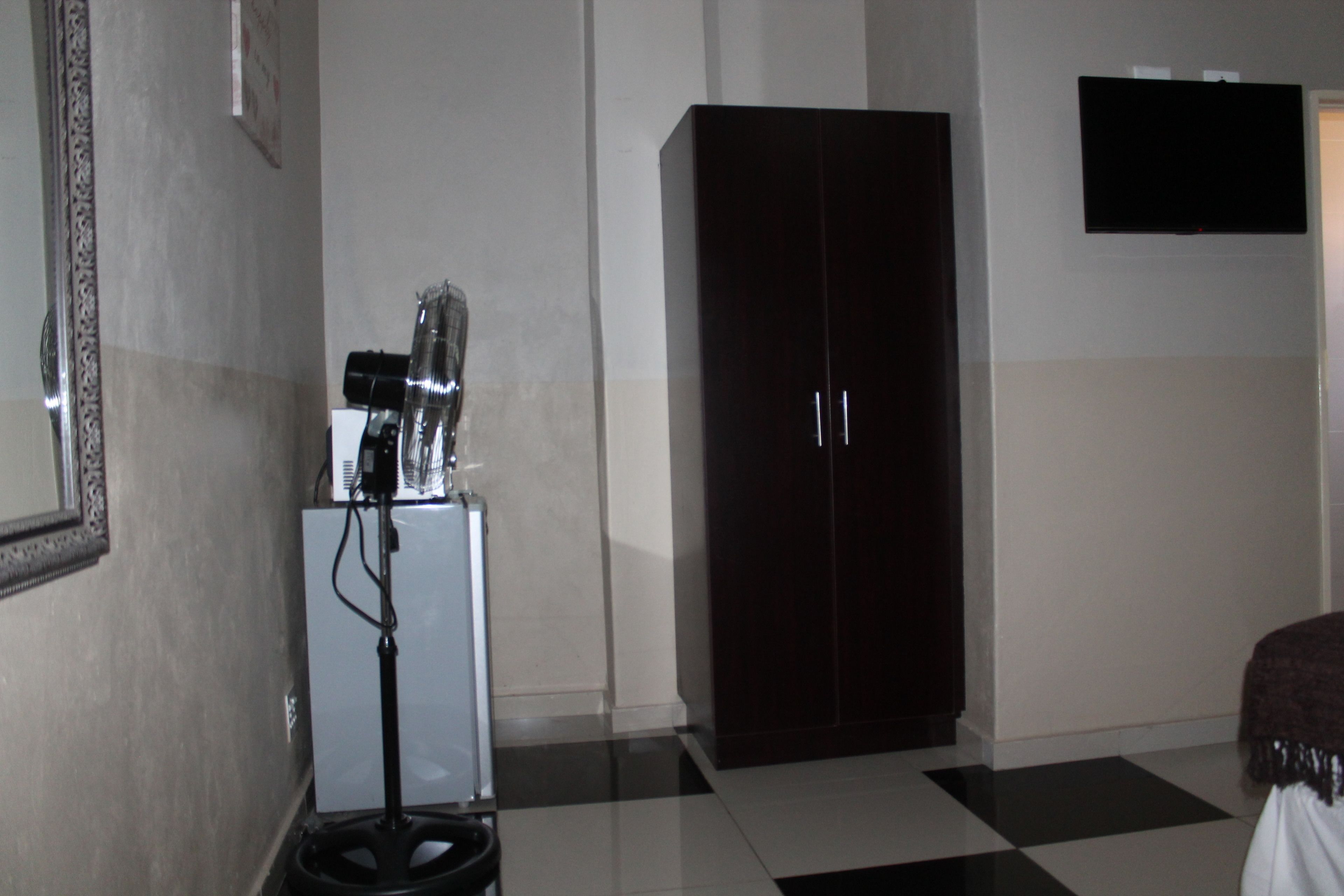 A room with a checkered floor, a dark wardrobe, a white cabinet, and a mounted television.
