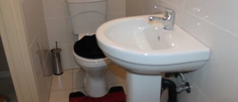 Un baño con un lavamanos blanco, un inodoro y una alfombra de baño roja y negra.