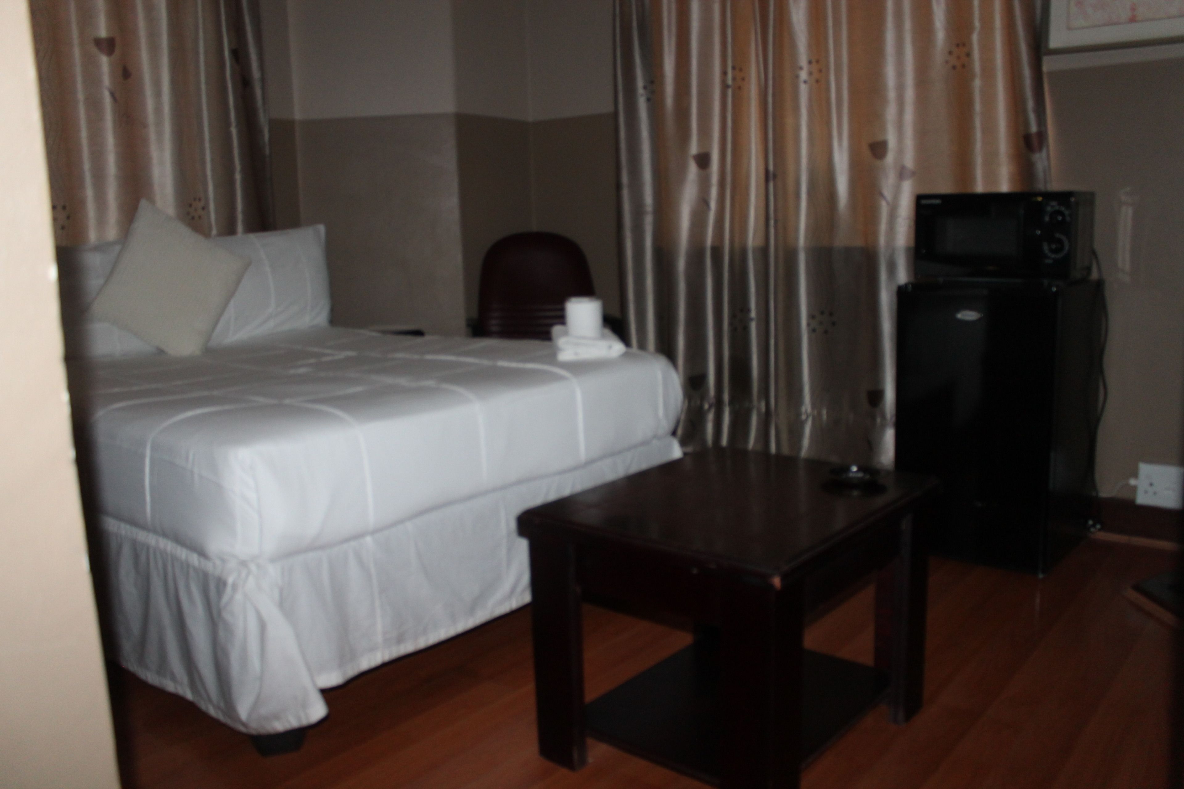 Quarto de hotel com cama, uma pequena mesa e um micro-ondas.