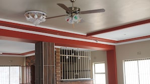 Ein Zimmer mit Deckenventilator, einer Chandelierleuchtre, einer Ziegelwand, vergitterten Fenstern und einer Farbgestaltung in Rot und Weiß.