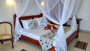 A bed with a canopy, white bedding, and a patterned throw. There is a chair and a nightstand with a lamp. - Ocean of Life Ayurvedic Resort (Bentota)