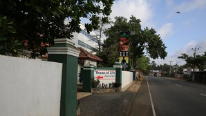 A road with a sign for Ocean of Life resort, a white building, and a green fence. - Ocean of Life Ayurvedic Resort (Bentota)
