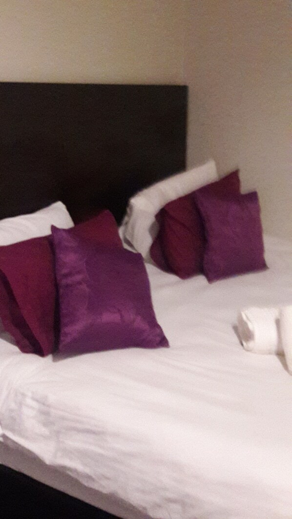A bed with white bedding and purple pillows.