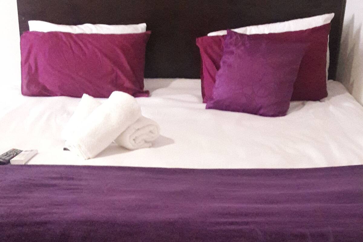 Un lit avec un drap blanc, deux oreillers violets et une couvre-lit violette.
