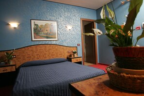 Quarto com cama, mesa de cabeceira, planta em vaso, quadro na parede e porta.