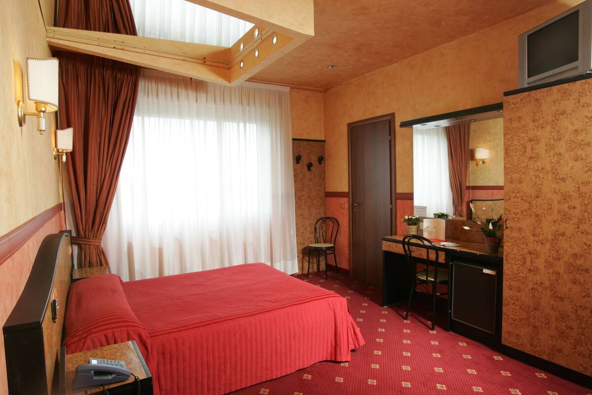 A hotel room with a bed, desk, chair, and a small cabinet.