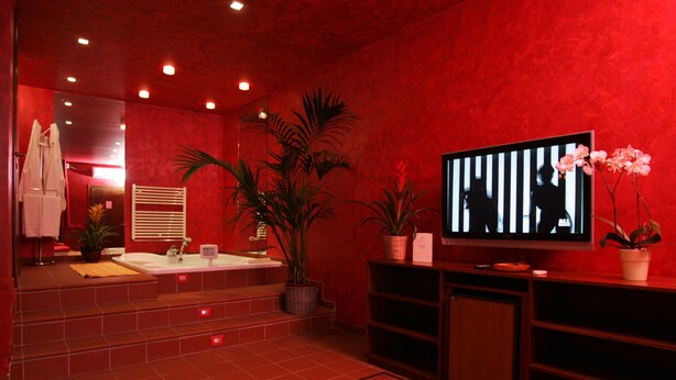 A red-walled bathroom with a large mirror, a sink, a bathtub, and a television. - Motel Ranch (Gaggiano)