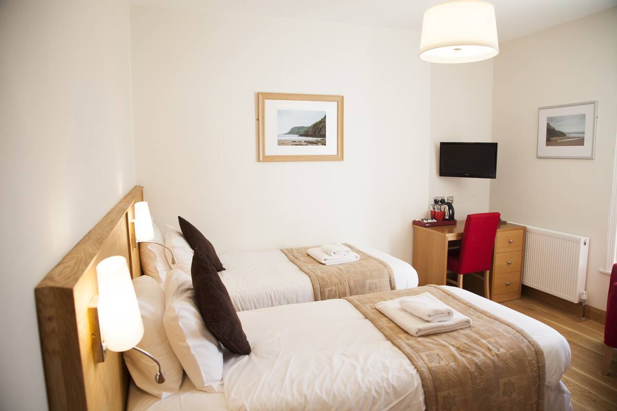 A hotel room with two beds, a desk, a chair, a TV, and framed pictures on the wall.