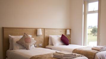 Une chambre d’hôtel avec deux lits, chacun doté d’une tête de lit en bois, de draps blancs et d’une fenêtre donnant sur l’extérieur.