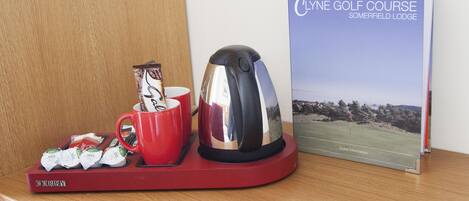 A red tray with a coffee pot and a red mug, a booklet titled "Clyne Golf Course," and a small stack of coffee packets.