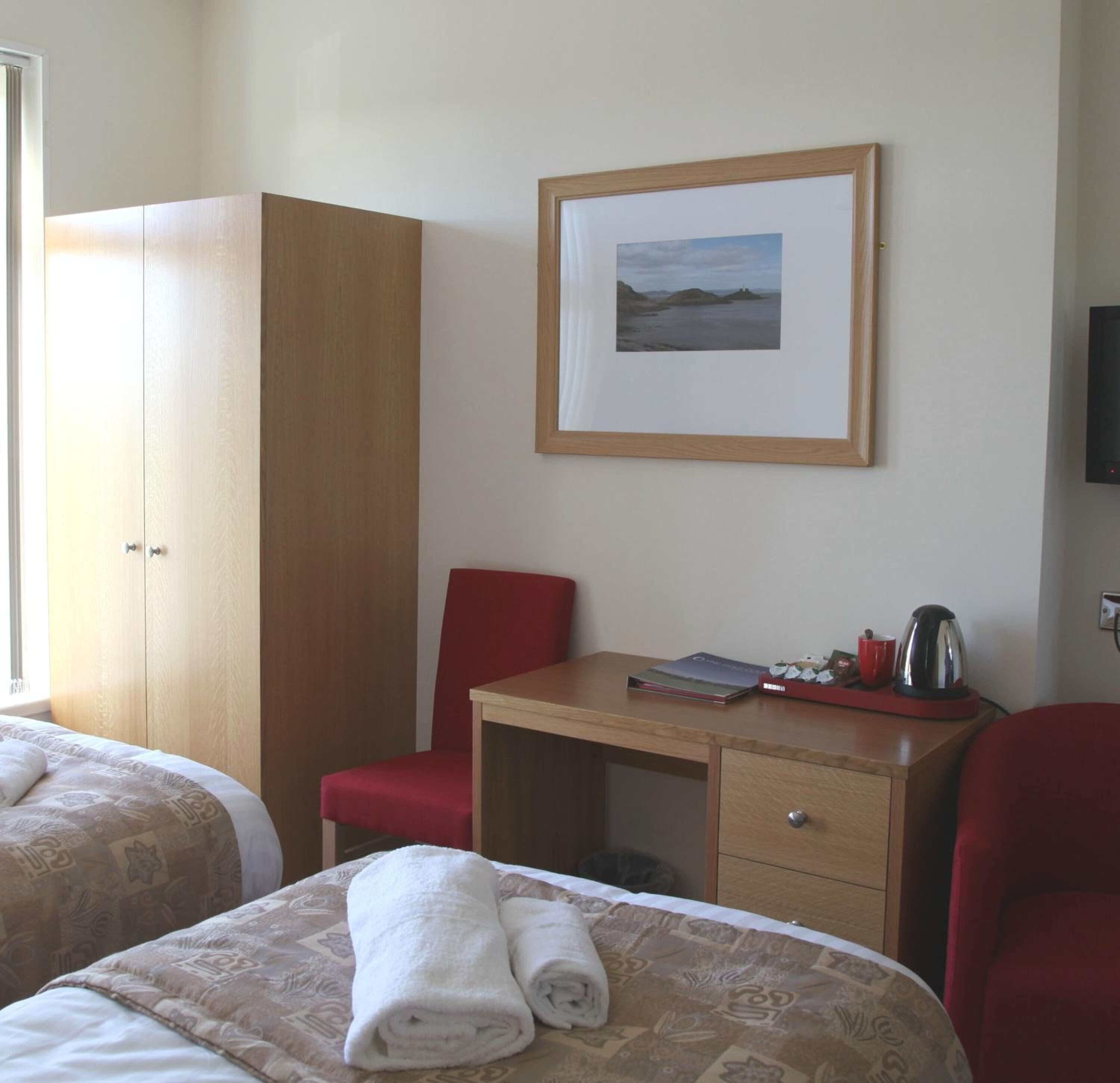 A hotel room with two beds, a wooden wardrobe, a desk with a chair, a framed picture on the wall, and a television.