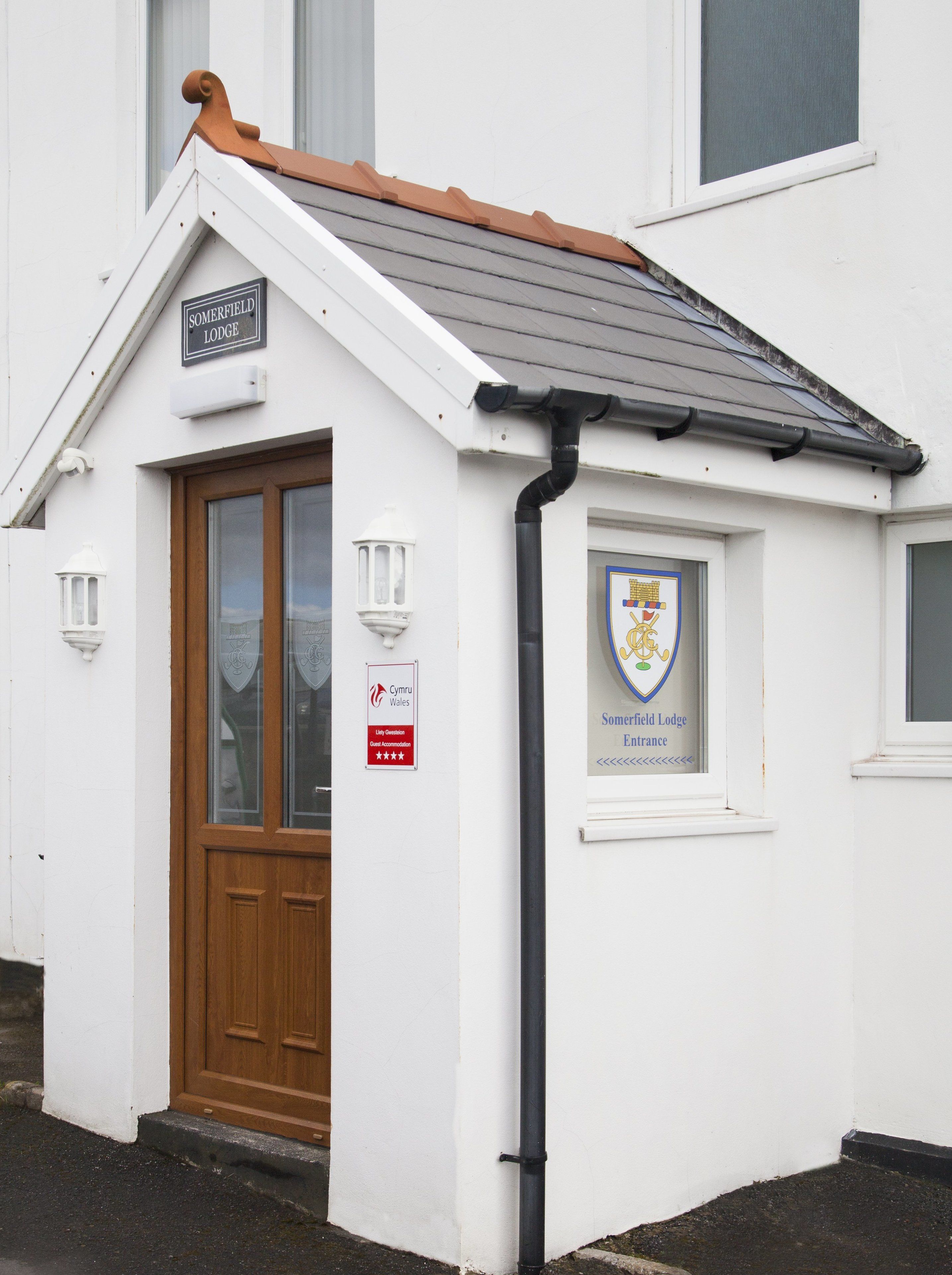 Un edificio blanco con una puerta marrón, un cartel que dice "Somerfield Lodge Entrance" y un emblema de escudo de armas.