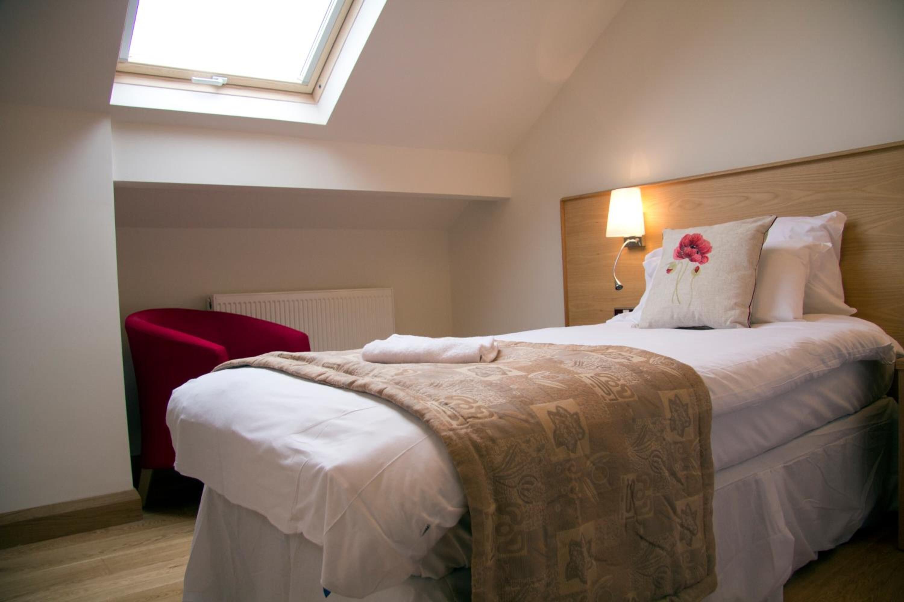 Ein Schlafzimmer mit Oberlicht, einem roten Sessel und einem Bett mit einem gemusterten Bettbezug.