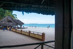 Uma praia com uma cabana de palha, uma cerca de madeira e uma área de areia.