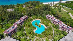 A resort with a central swimming pool, multiple buildings, and a beach.