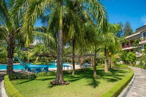 Uma área de piscina com palmeiras, piscina e um edifício com varandas.