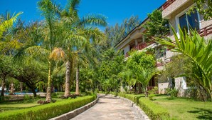A pathway lined with palm trees and well-maintained grass, leading to a building with a stone facade and red railings.