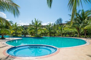 Uma piscina ampla e convidativa, rodeada por palmeiras e um deck revestido com azulejos.