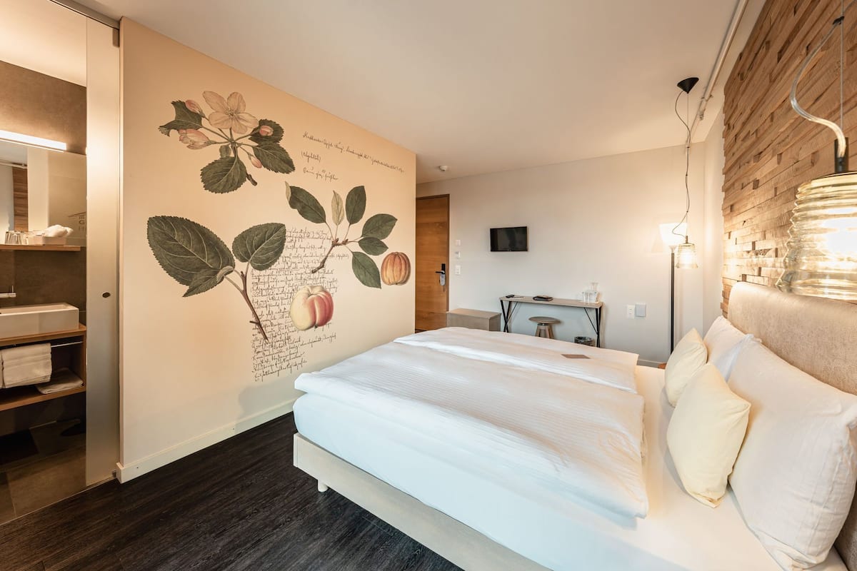 A hotel room with a large bed, a desk, a television, and a wall with botanical illustrations.