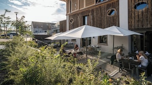 Un espace extérieur aménagé en terrasse, avec des tables et des chaises sous des parasols, entouré de verdure.