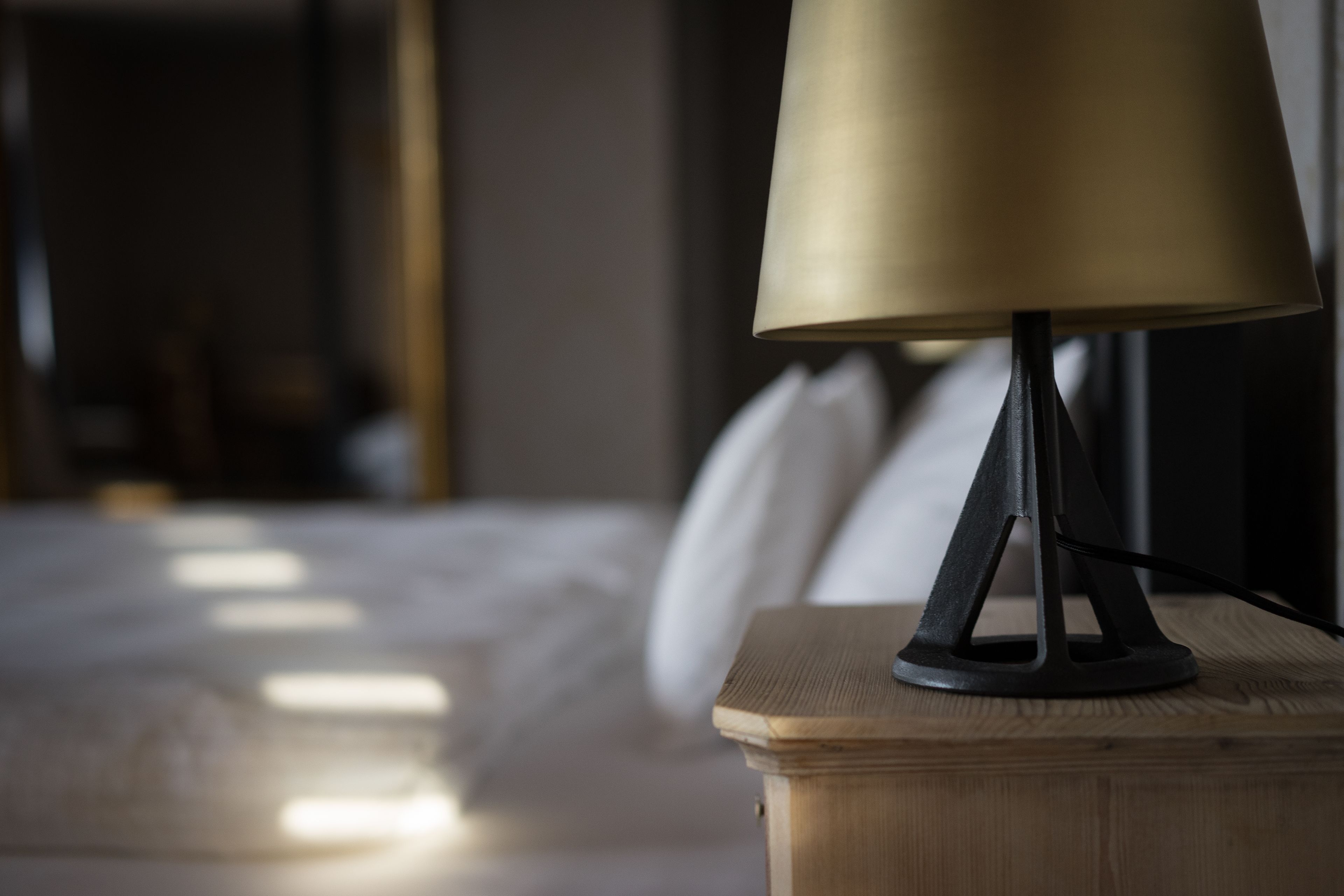 A bedside table with a lamp, a bed, and pillows in a hotel room.