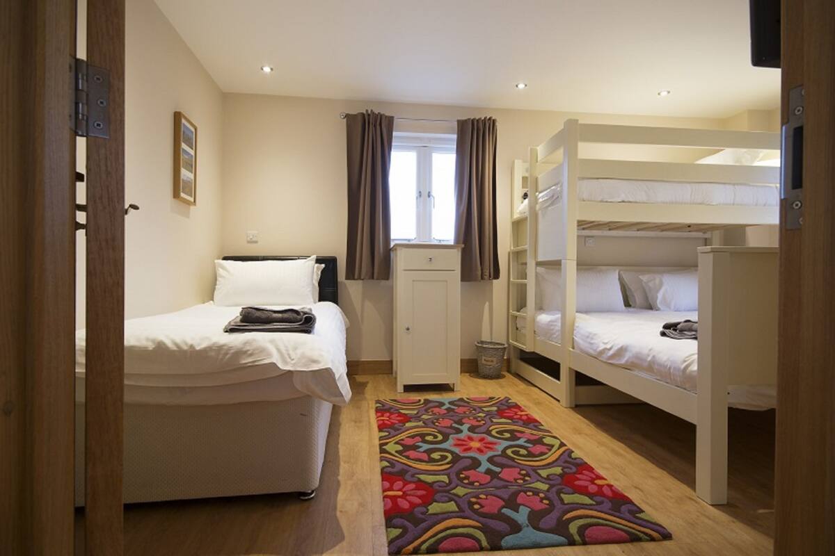 Une chambre avec un lit simple, un lit superposé, une petite armoire et un tapis coloré.