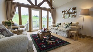 A cozy living room with a large window, a wooden ceiling, and a floral rug. - Tynrhyd Retreat (Aberystwyth)