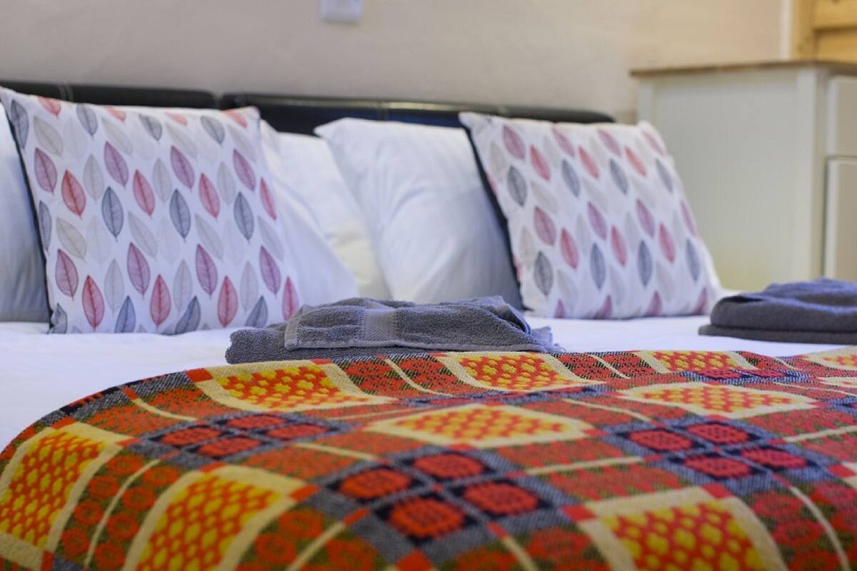 Un lit avec des coussins à motifs, une couverture colorée et un couvre-lit soigneusement disposé.