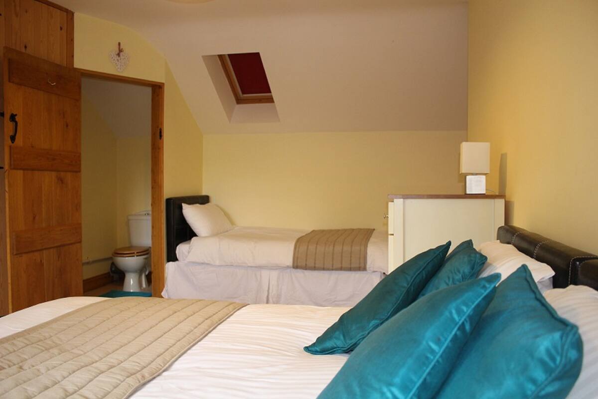 Une chambre avec deux lits, une armoire en bois, une petite fenêtre et une table de chevet avec une lampe.