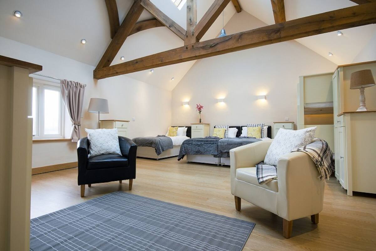 Une chambre spacieuse de style « loft », avec des poutres apparentes, deux lits, un canapé et un coin bureau.