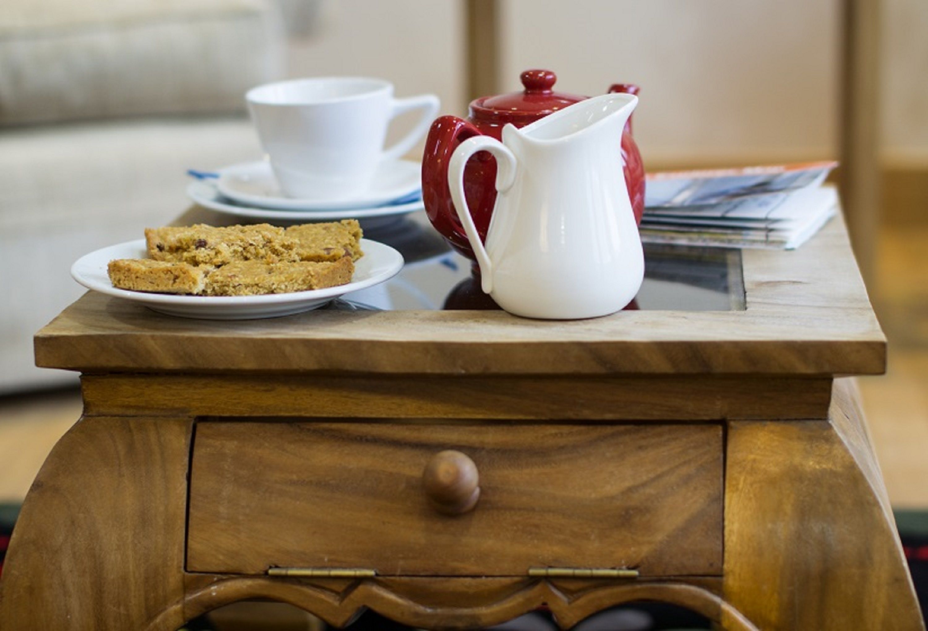 A wooden table with a white pitcher, a teapot, a cup, and a plate of cookies.
