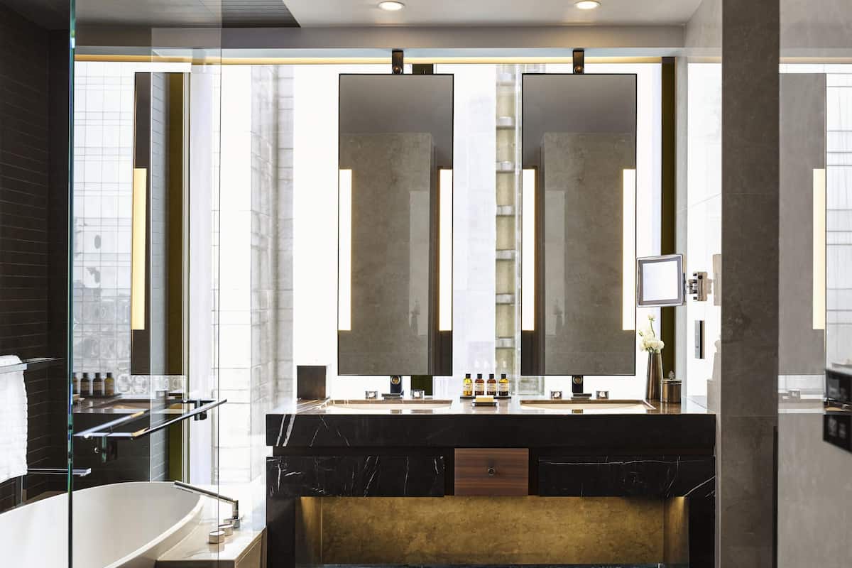 Une salle de bain moderne avec un grand miroir, une baignoire et un meuble-lavabo agrémenté d’un mur d’accent doré.