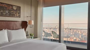 A hotel room with a large bed, a city view through the window, and a small table with chairs.