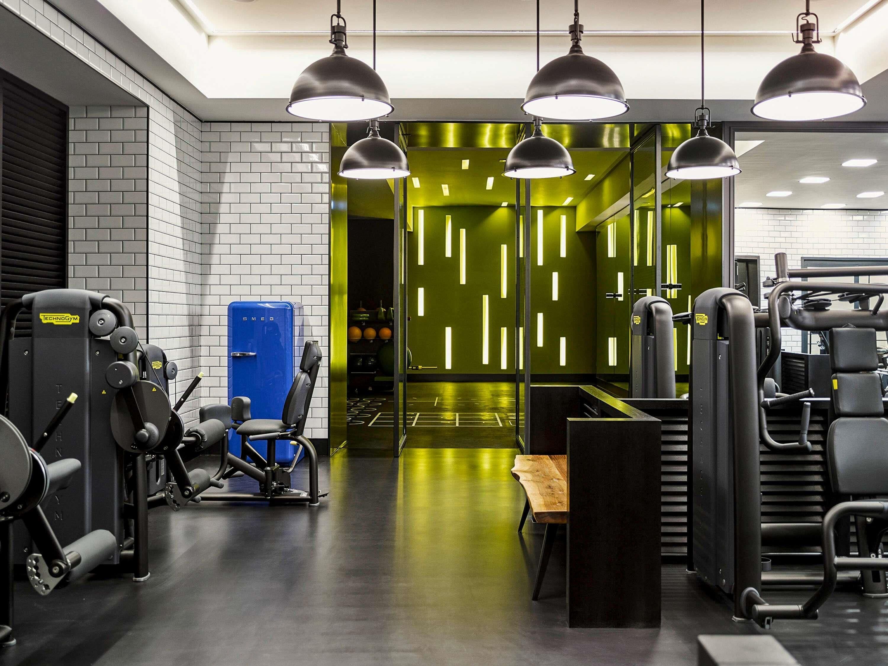 A modern gym with various exercise machines, a blue water cooler, and pendant lighting.