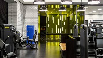 A modern gym with various exercise machines, a blue water cooler, and pendant lighting.