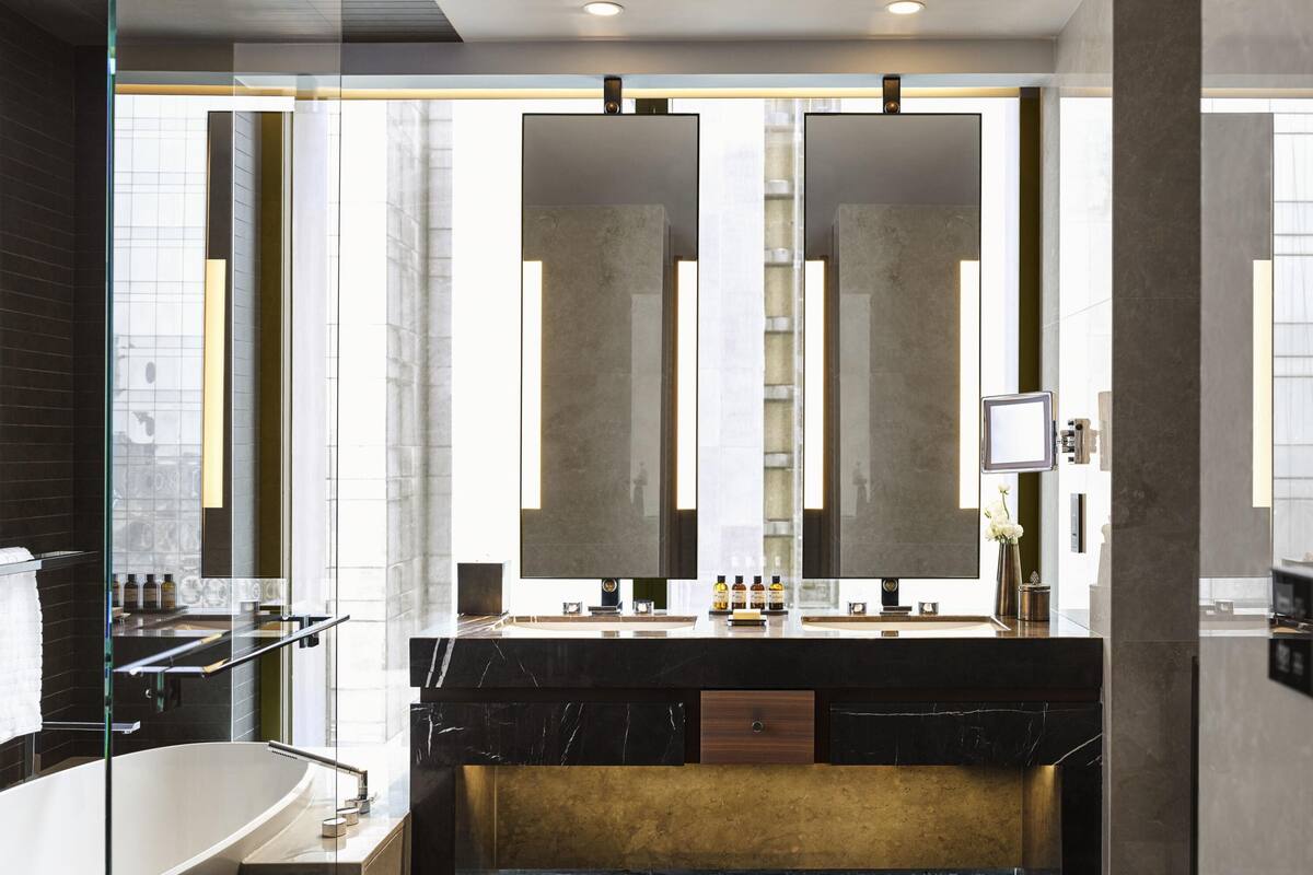 A modern bathroom with a large mirror, a bathtub, and a vanity with a gold accent wall.