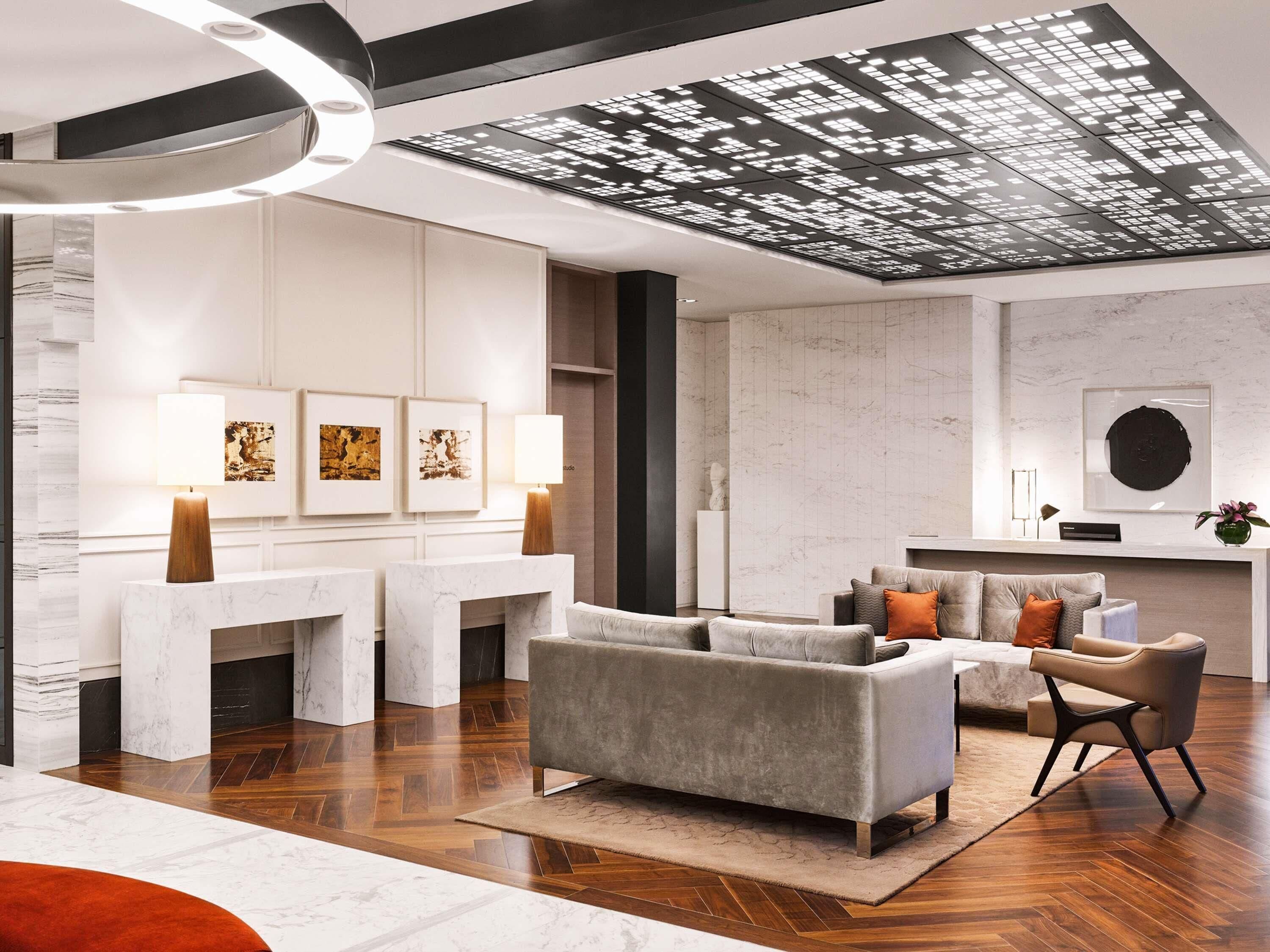 A modern interior with a marble reception desk, grey sofas, and a unique ceiling design.