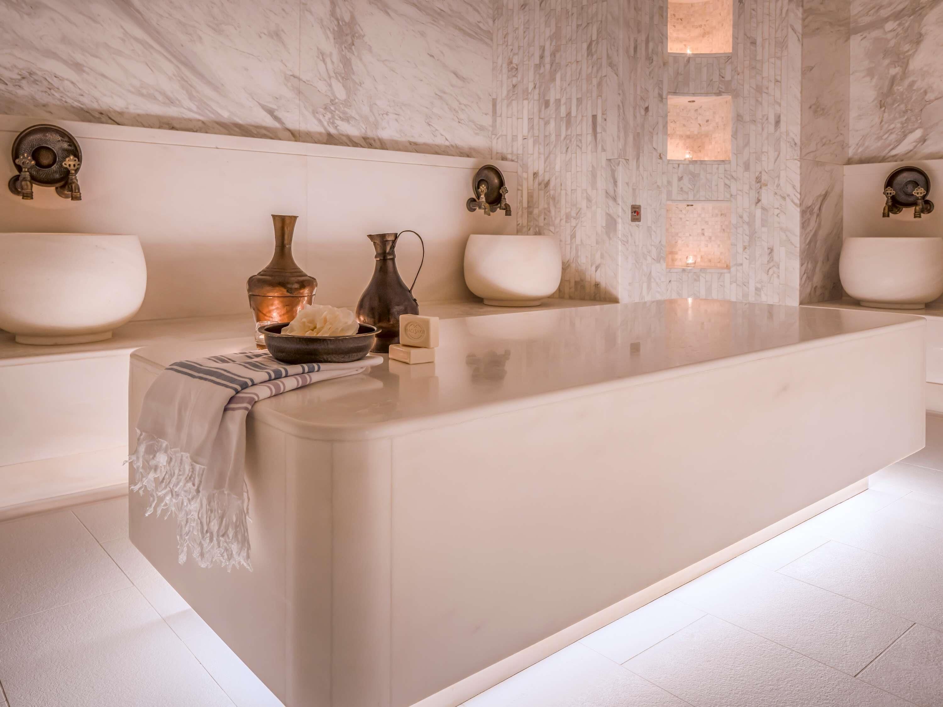 A modern bathroom with a marble wall, a large central sink, and two wall-mounted toilets.