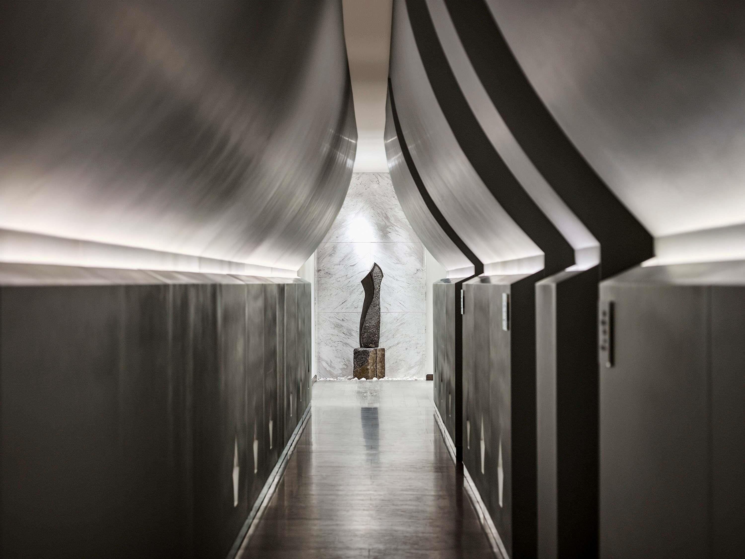 A corridor with metallic walls and a marble floor, leading to a central point with a stone sculpture.