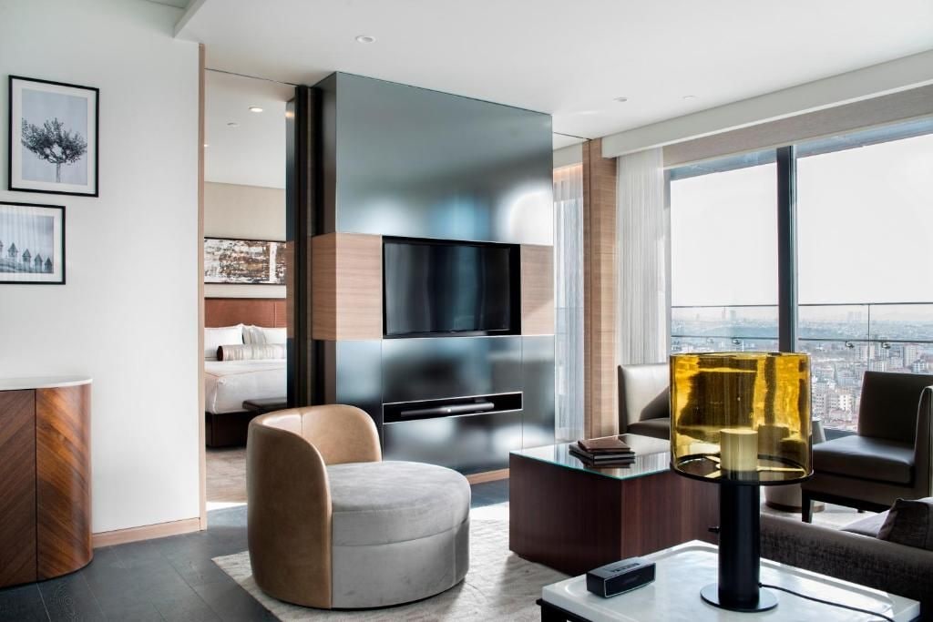 Ein modernes Wohnzimmer mit Flachbildfernseher, rundem Hocker, Glastisch und Blick auf die Stadt.