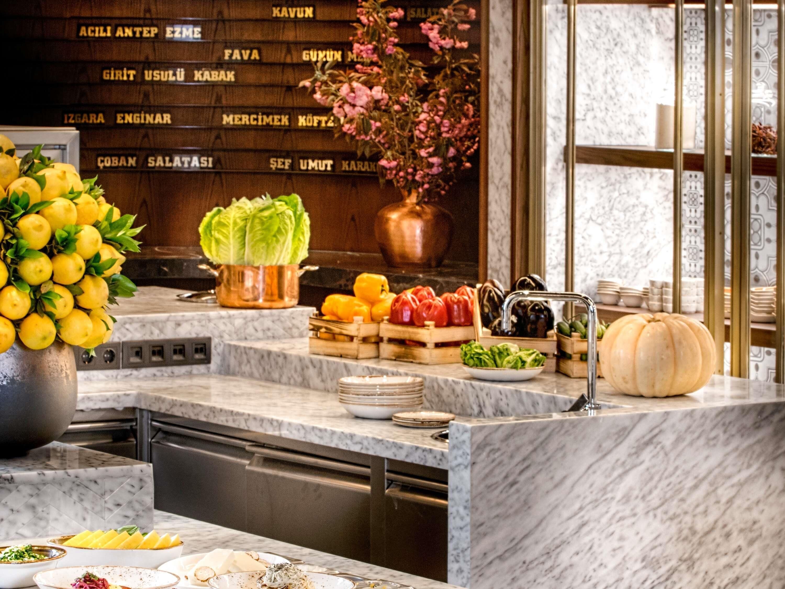 A kitchen with marble countertops, a variety of fresh produce, and a copper pot on the counter.