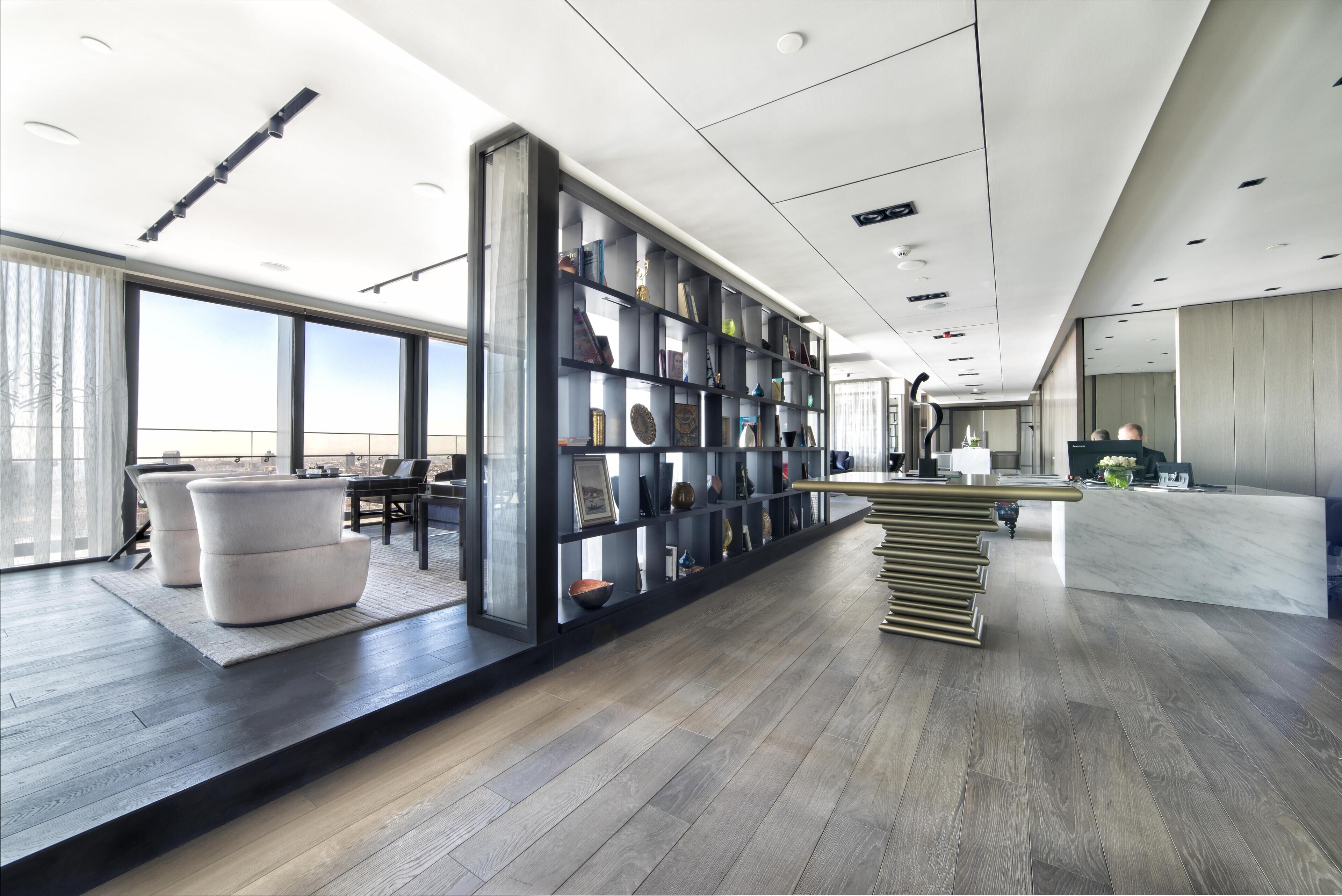 Un hall d’hôtel moderne, doté d’une grande bibliothèque, d’un comptoir d’accueil et d’un espace détente avec des canapés.